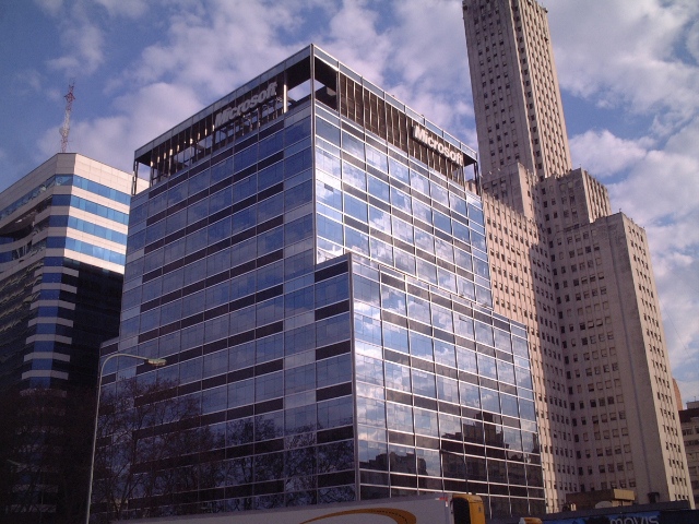 A tall glass building with the Microsoft logo at the top and a cloudy sky